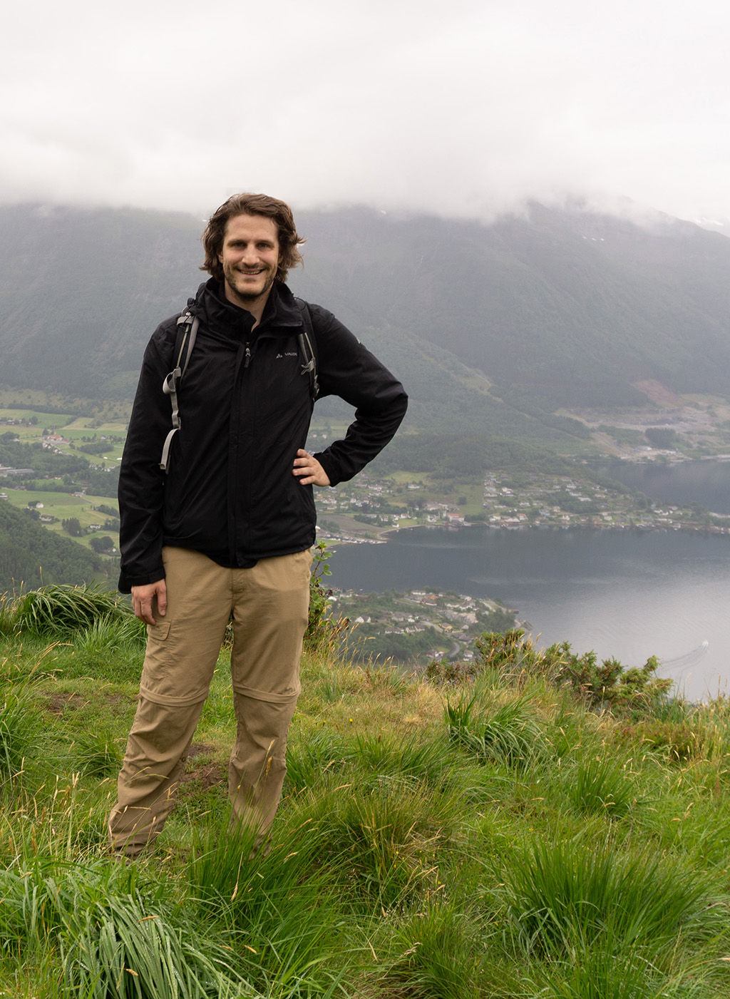 The picture shows Konstantin on a mountain with fjord and fog in the background during a hiking tour in Norway.