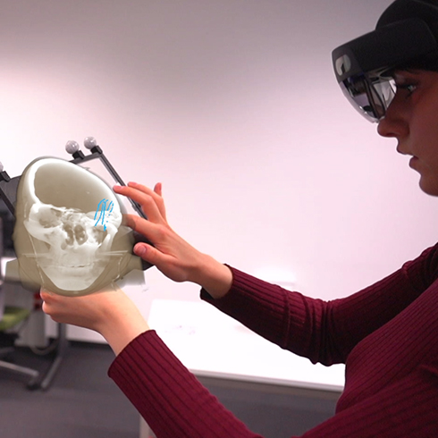 The image shows how a user interacts with the CleAR Sight prototype and a HoloLens. In detail, a woman holds the transparent tablet in her hands while she is annotating a specfic region of a MRT scan.