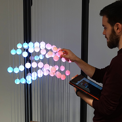 The picture shows the STRAIDE installation in action with a user who interacts with the data sculpture by touch a illuminated sphere.